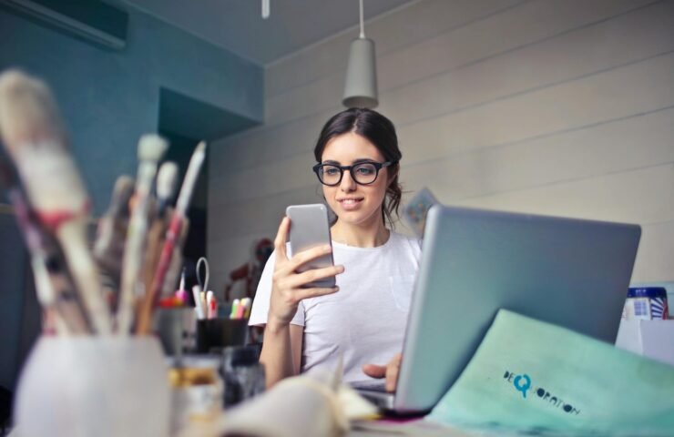 woman in white t shirt holding smartphone in front of laptop